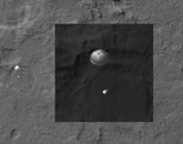 A black and white image showing Curiosity and its parachute as the rover was landing. The Descent of Curiosity: NASA’s Mars Science Laboratory, Curiosity, was spotted by HiRISE as it descended to the surface on Aug. 5, 2012. Curiosity and its parachute are on the left, while above is a close-up, stretched to avoid saturation. The rover is landing on the etched plains just north of the sand dunes that fringe Aeolis Mons (informally called Mount Sharp) within Gale Crater.